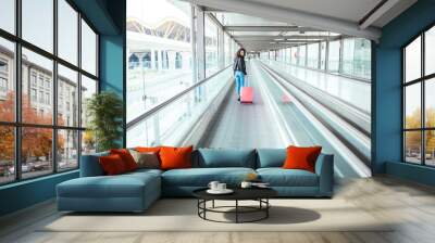 black woman in the moving walkway at the airport with a pink suitcase. Wall mural