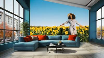 Happy young black woman walking in a sunflower field Wall mural