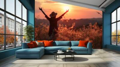 Silhouette photo of one woman standing in outdoor grasses field raising two hands in the air showing freedom relax emotion at twilight time with beautiful sunset. Wall mural