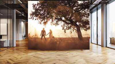 groom and bride in a wedding dress going through the field on a background of  sunset. Wall mural