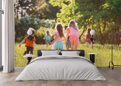 Large group of kids, friends boys and girls running in the park on sunny summer day in casual clothes . Wall mural