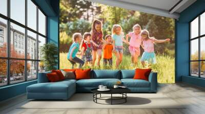 Large group of kids, friends boys and girls running in the park on sunny summer day in casual clothes . Wall mural