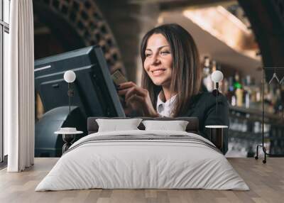 small business, people and service concept - happy woman or waiter or manager in apron at counter with cashbox working at bar or coffee shop Wall mural