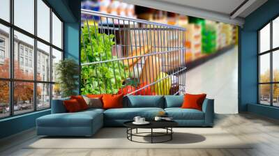 Shopping cart full of food in supermarket aisle side tilt Wall mural