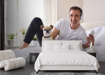 Smiling man listening music lying in bed with chihuahua Wall mural