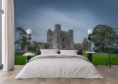 Beautiful old ruins of christian Bective Abbey from 12th century with green trees, pasture and moody dark sky in the background, County Meath, Ireland Wall mural