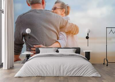 Retirement couple sitting by the sea, women embrace husbands and look at each other at the beach in the morning, life insurance plan at the retirement concept. Wall mural