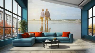 Senior couple walking on the beach holding hands at sunrise, plan life insurance at retirement concept. Wall mural