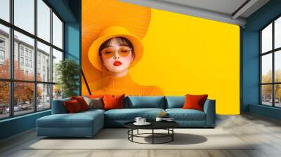 A stylish woman in vibrant yellow attire poses gracefully with a matching umbrella against a bright yellow backdrop. Wall mural