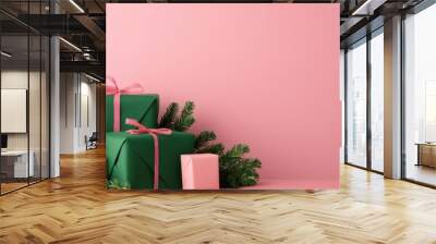 Colorful holiday gifts with ribbons and greenery, set against a soft pink background, perfect for festive decorations. Wall mural