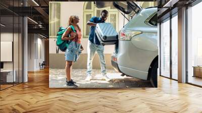 African american partners travelling by vehicle, putting luggage and baggage in trunk to leave on summer holiday. People in relationship going on vacation trip with trolley and travel bags. Wall mural