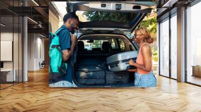 African american people loading baggage in automobile to leave on holiday vacation trip. Partners travelling by car with luggage, suitcase and bags to go to summer adventure cityscape. Wall mural