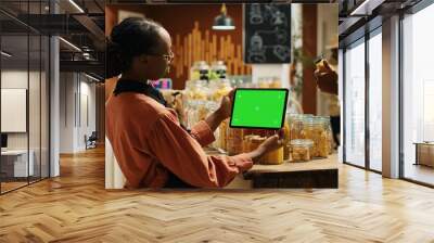 African american woman uses greenscreen on tablet in supermarket, standing next to natural organic products. Female vendor holding gadget showing isolated copyspace mockup layout. Camera 1. Wall mural