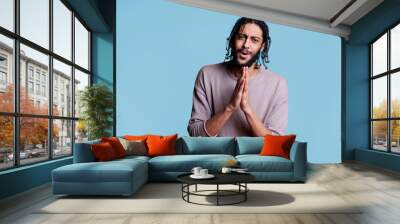 Arab man pleading with folded hands and hopeful facial expression portrait. Young adult person begging and looking at camera with pleading emotions while posing for studio shot Wall mural