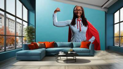 Arms muscle flexing brave superhero woman posing strong and tough for camera on blue background. Justice defender wearing mighty hero red cape while expressing empowerement. Studio shot. Wall mural