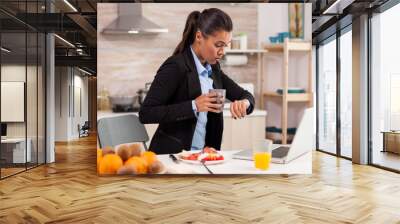 Caucasian businesswoman late to the office in the morning, eating in the hurry and looking at the watch Wall mural