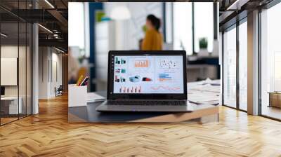 Close up of laptop in start up company office with charts and statistics. Workplace area in business center with multi ethnic employees in it, shot of room with modern furniture and blue wall. Wall mural