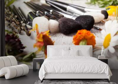 cosmetic make up brushes next to wild flowers on wooden background Wall mural