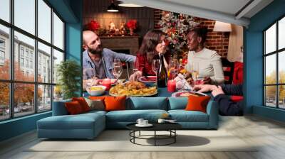 Couple celebrating christmas with parents and friends, wife and husband talking with african american woman at festive dinner table. Xmas celebration, diverse people gathering on holidays Wall mural