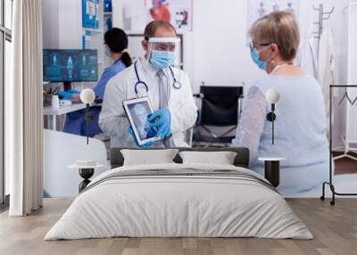 Doctor using tablet pc during examination of x-ray for older patient in hospital room and wearing face mask against coronavirus pandemic. Medical examination for infections, disease and diagnosis. Wall mural