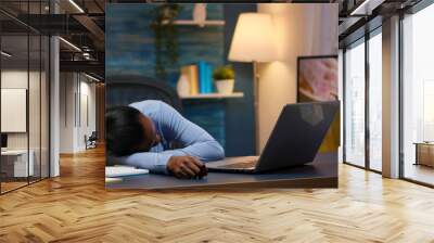 Exhausted overload black businesswoman falling asleep on desk with open laptop monitor while working from home. Busy employee using modern technology network wireless doing overtime sleeping on table. Wall mural