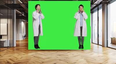 General practitioner with a white coat using stethoscope in studio, preparing to examine patients at checkup appointments. Female doctor in uniform standing against greenscreen backdrop. Camera A. Wall mural