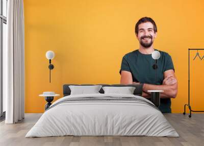 Handsome man with his arms crossed smiling at the camera isolated on yellow background. Portrait of attractive bearded confident person in studio photo Wall mural