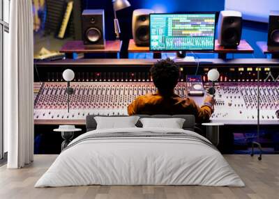 Joyful sound designer finishing a new hit song in music recording studio, working with digital audio software and console in control room. Technician producing records with soundboard panel. Wall mural