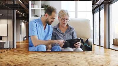 Male assistant teaching senior retired elderly old woman how to use her tablet computer in nursing home for her therapy Wall mural