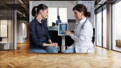 Medical laboratory worker delivering x ray images to young female patient. Medical surgeon explaining medical procedure to cure woman disease in medical clinic waiting room. Wall mural