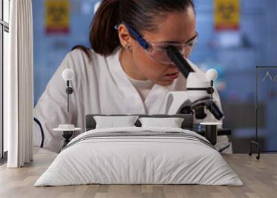 Medicine researcher woman working with microscope in chemical laboratory at medical clinic. Professional analysis worker using biotechnology equipment for discovery treatment development Wall mural