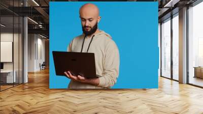 Middle eastern man works with cyber security on laptop, trying to do some software programming and report bugs. Young adult operating as a system developer in studio. Camera 2. Handheld shot. Wall mural