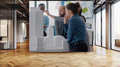 Multi ethnic people working with building model to design urban architectural project. Architects colleagues using maquette to plan construction layout and blueprints, doing teamwork. Wall mural