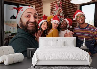 Multiethnic group of people taking pictures with tree, celebrating festive season with christmas holiday decorations in business office. Colleagues taking photos with seasonal xmas ornaments. Wall mural