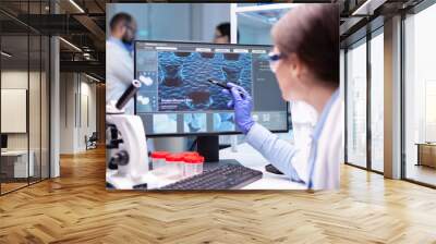 Professional biochemist analysing a medical experiment while working with her team to discover a vaccine. Healthcare physician pointing at virus on computer. Wall mural