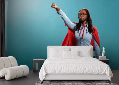 Proud and strong african american justice defender looking ambitious while looking at camera. Powerful and brave young superhero woman wearing hero costume while posing as flying on blue background. Wall mural