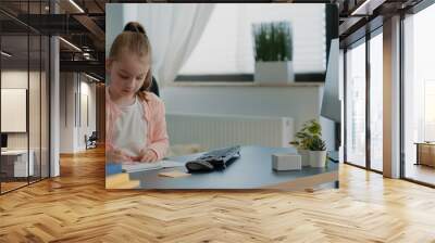 Schoolgirl drawing on notebook with colorful pencils and using computer for homework and online courses. Little child with textbook looking at monitor for remote lessons and education Wall mural