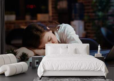 Sleepy employee asleep on computer desk late at night in brick wall office. Panning shot of tired businesswoman sleeping with head on table while working overnight on laptop, camera B Wall mural