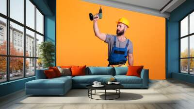 Young carpenter working wtih electric power drill tool, wearing overalls and holding drilling gun. Handyman contractor using cordless drill to work on renovation and refurbishment. Wall mural