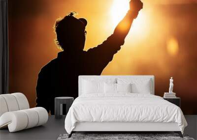 Silhouette of a man raising his fist in determination during sunset, symbolizing empowerment and activism, with a dramatic light background.
 Wall mural