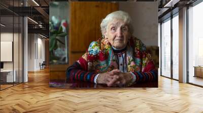 an elderly woman in slavic clothes sitting in home. Wall mural