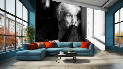 An elderly woman sadly looking out the window, a black-and-white photo. Wall mural