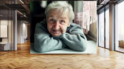 An old elderly woman, smiling portrait, looking at the camera, sitting in the kitchen. Wall mural