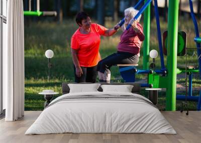 Elderly woman is doing exercises on the sport playground in the Park. Wall mural