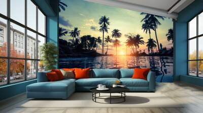 Tropical beach with pool and silhouetted palm trees during sunset. Wall mural