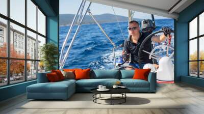 Young man steers a sailing yacht boat in the open sea. Wall mural