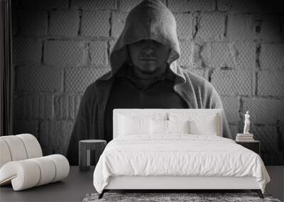 Black and white photo of a man in a cardigan with a hood on his head against a brick wall Wall mural