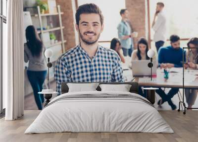 All for one and one for all! Leadership. Successful stylish young bearded man in casual checkered shirt is standing in the office, smiling, making notes Wall mural