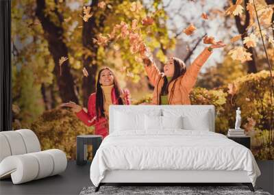 Autumn weekend fun time concept. Positive girls buddies enjoy throw catch air fly maple leaves wear red yellow outerwear in sunset forest park lawn Wall mural