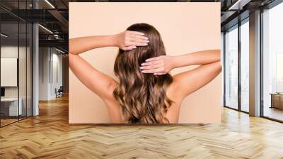 Back view photo of young beautiful woman washing wavy brown hair with shampoo isolated on beige color background Wall mural